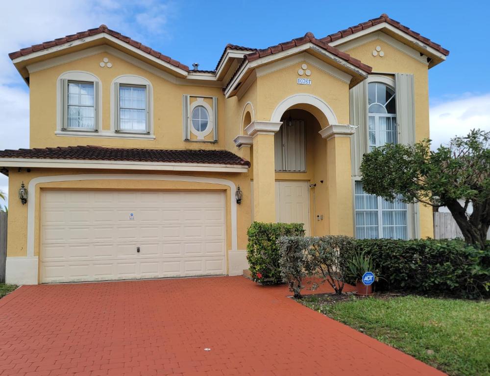 a yellow house with a garage on a brick driveway at My Florida Lake House in Homestead