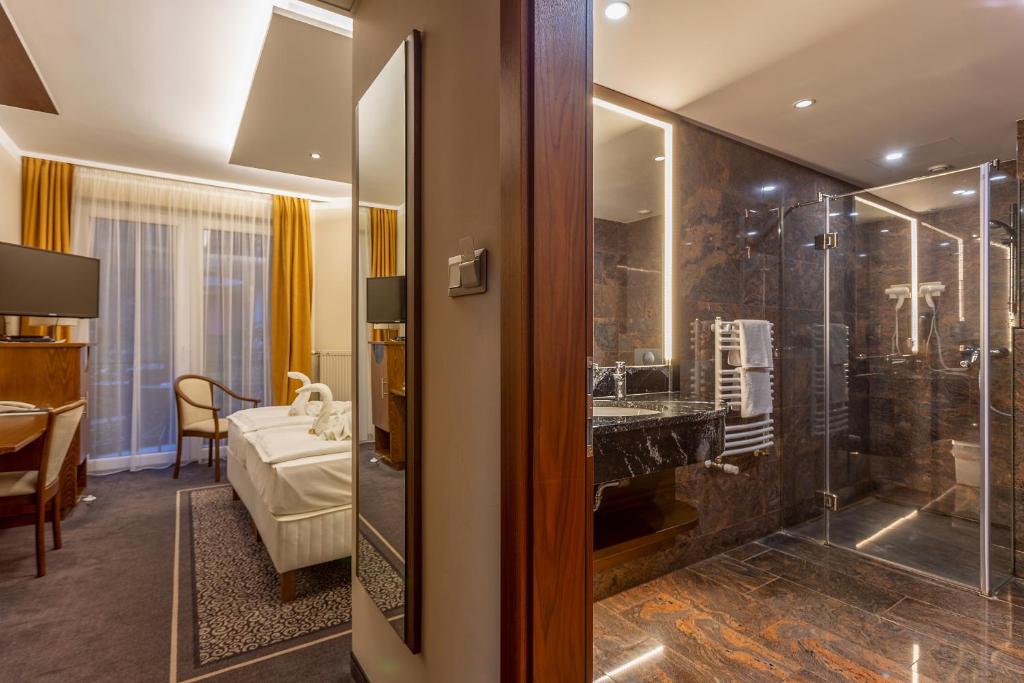 a bathroom with a glass shower and a bedroom at Szőnyi Garden Hotel Pest in Budapest