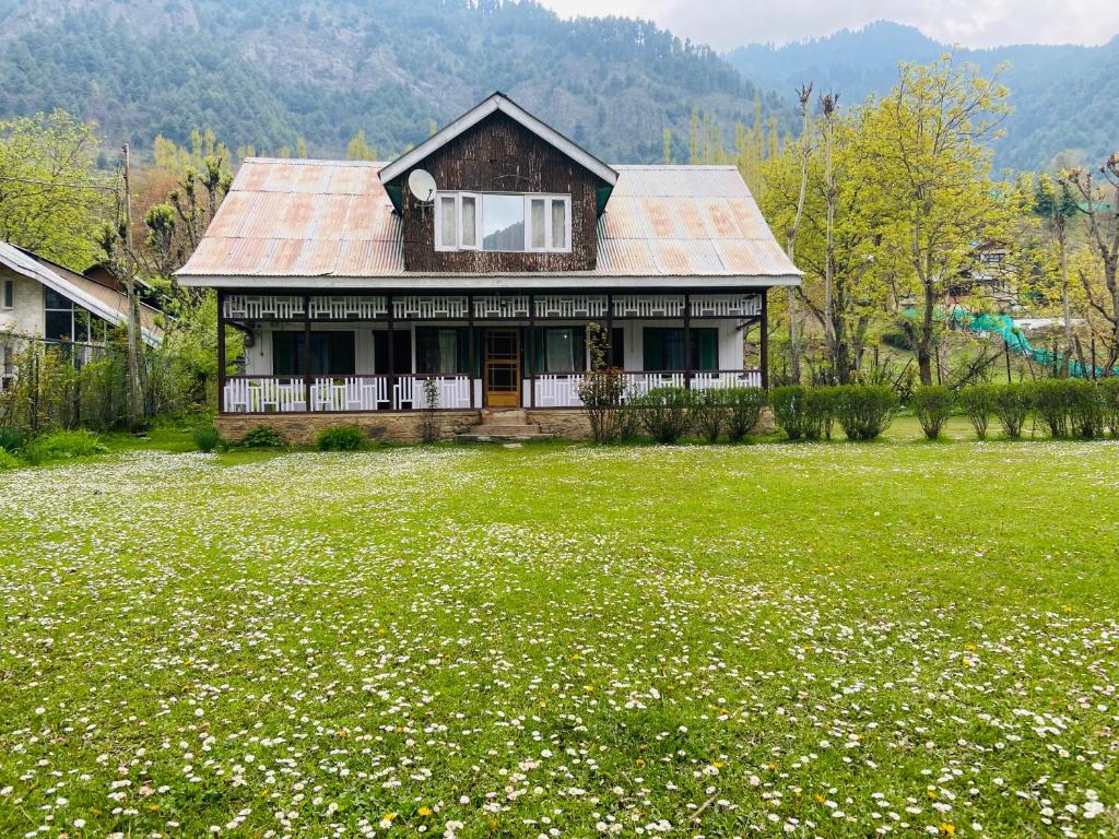 a house in a field of green grass with white flowers at PK cottage in Pahalgām
