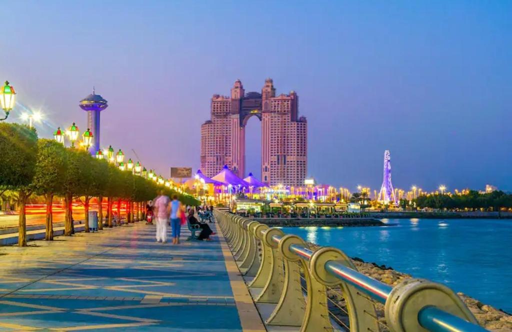 people walking on a sidewalk next to a river with buildings at Corniche AD - For Males "Peaceful Bed Space" in Abu Dhabi