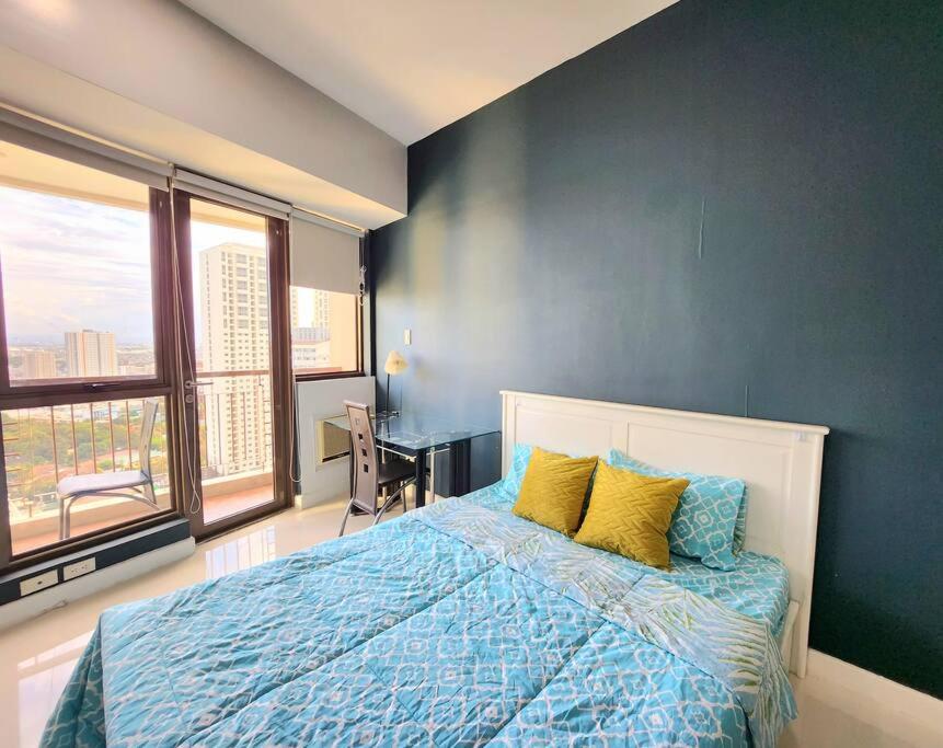 um quarto com uma parede azul e uma cama com almofadas amarelas em Nice and Cozy Studio near Greenbelt Makati with Balcony em Manila