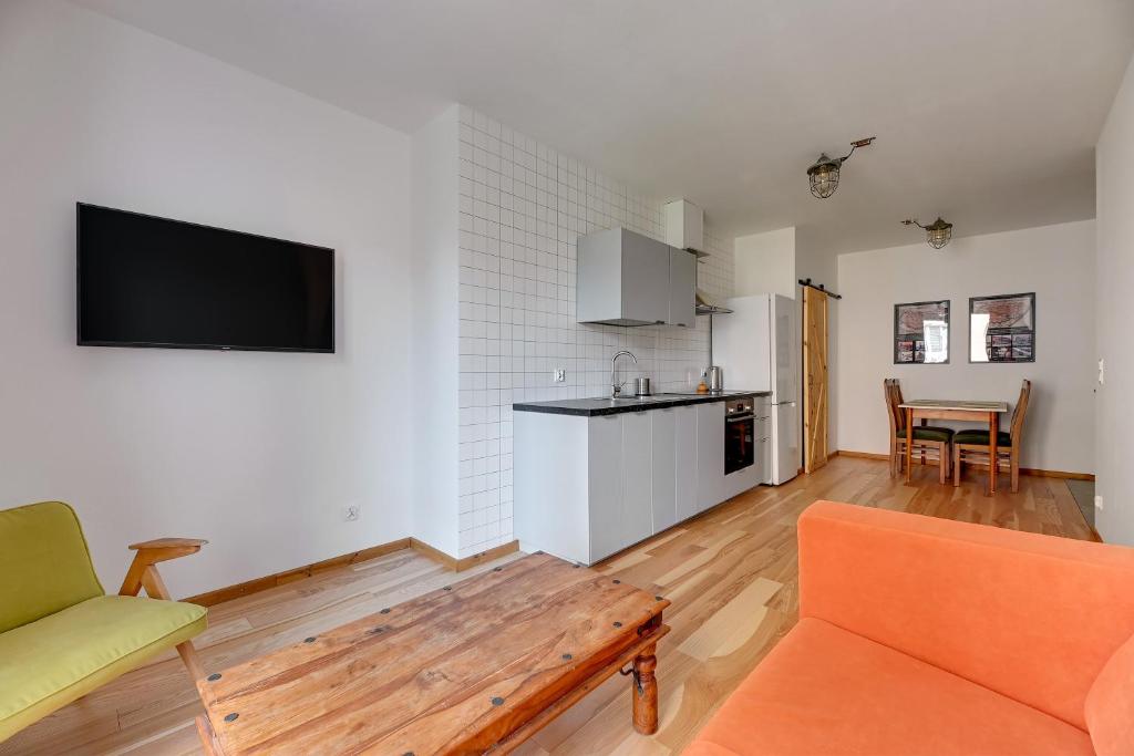 a living room with an orange couch and a kitchen at Staywin WILCZA apartments in Gdańsk