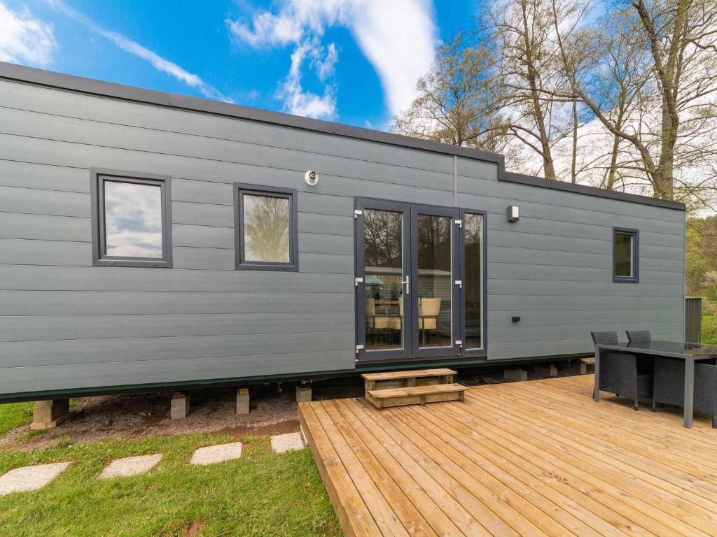 een grijs tiny house met een houten terras bij Brand new spacious mobile home with private terrace, next to a babbling brook in Érezée