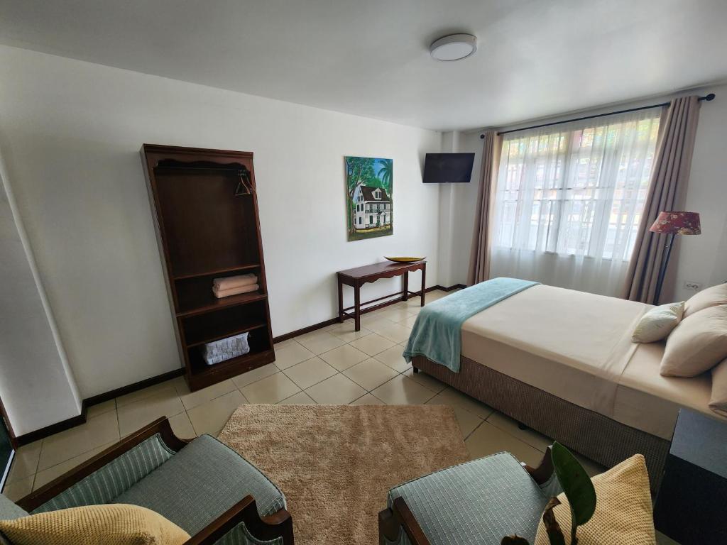um quarto com uma cama, uma televisão e uma cadeira em Queen Maxima by Prins Hendrik Suites em Paramaribo