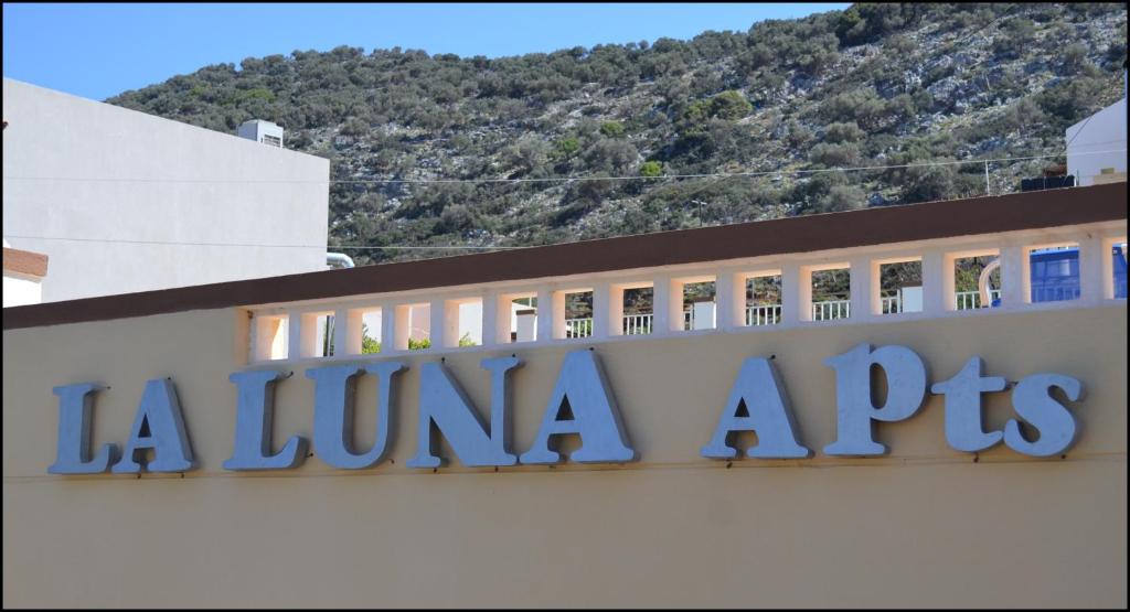 ein Schild auf einem Gebäude mit einem Berg im Hintergrund in der Unterkunft La Luna Apartments in Stalida