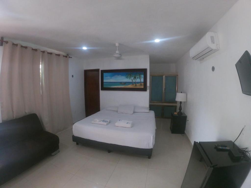 a bedroom with a bed and a couch and a television at Villas Karalv in Bacalar