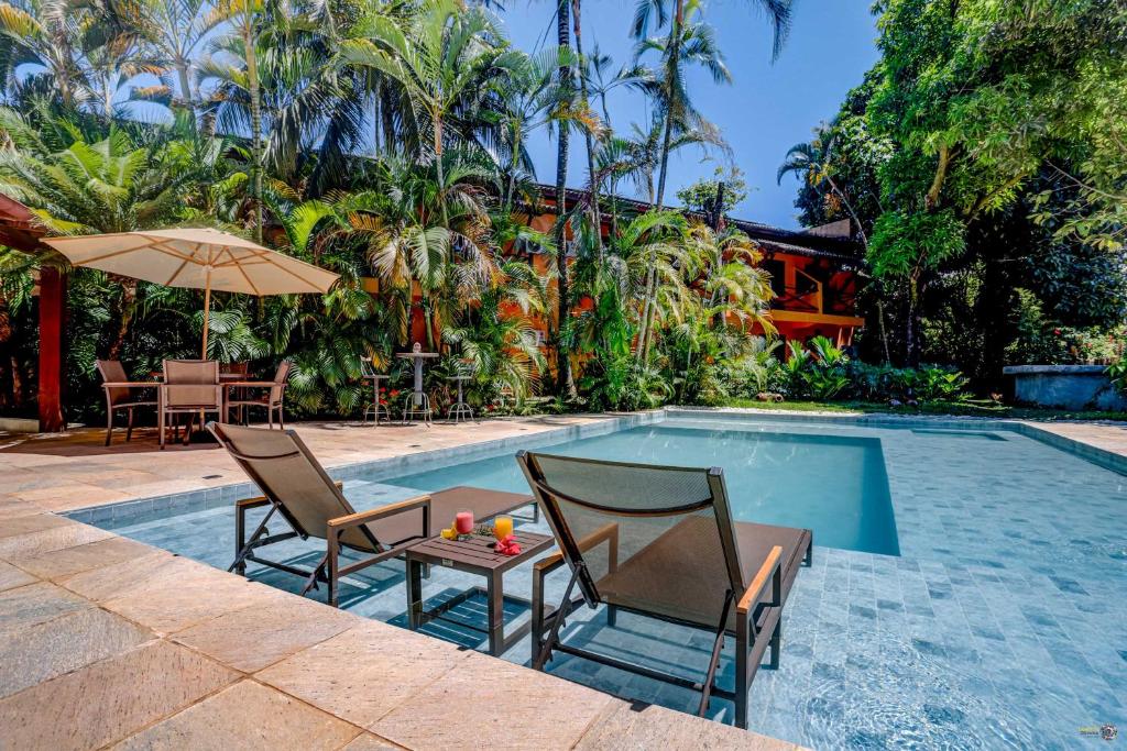 uma piscina com duas cadeiras, uma mesa e um guarda-sol em Pousada Villa N'kara em Itacaré