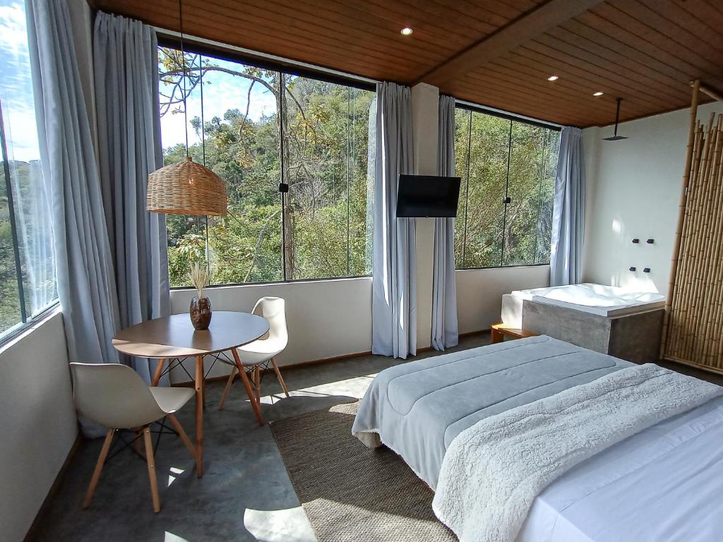 ein Schlafzimmer mit einem Bett und einem Tisch sowie einigen Fenstern in der Unterkunft Vista do Vale lofts - Itaipava in Petrópolis