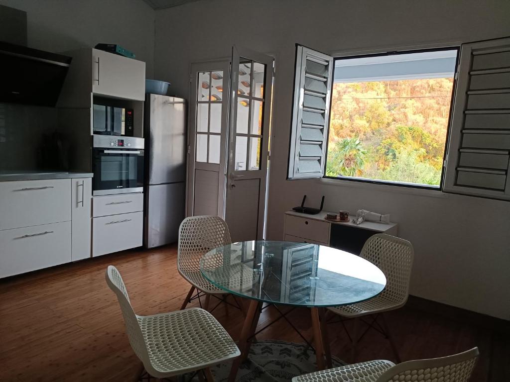 een keuken met een glazen tafel en stoelen en een raam bij Rêves de rivière- fonctionnel et bien placé in Le Carbet
