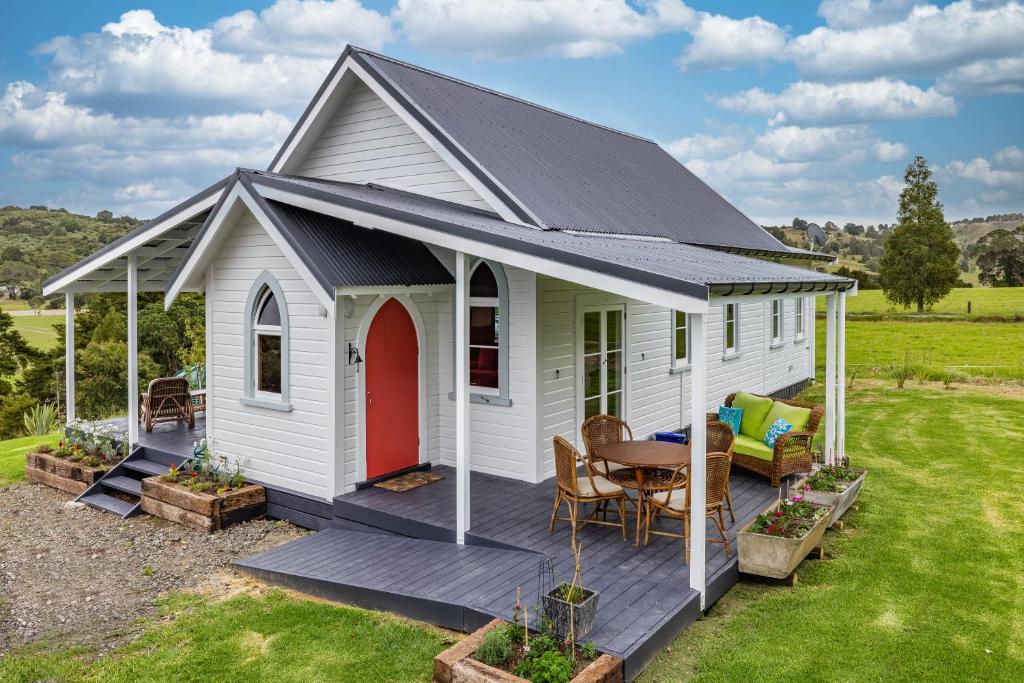 a white tiny house with a red door and a table at The Chapel- Kohukohu in Kohukohu Town District