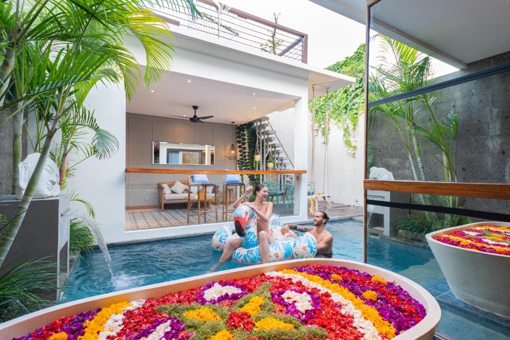 two people sitting in a pool with a large tub of flowers at Ayona Villa Seminyak by Ini Vie Hospitality in Seminyak