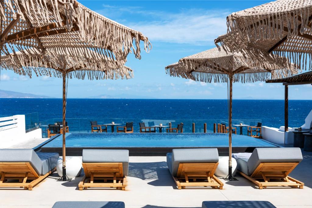 una piscina con sillas y sombrillas y el océano en Almyra Oia Suites, en Oia