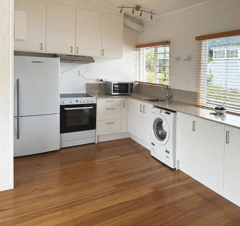 cocina con armarios blancos, lavadora y secadora en Home on The Grange in Mt Eden, en Auckland