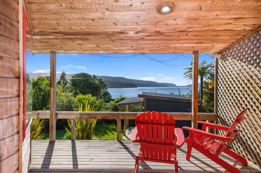 a deck with two red chairs and a view of the water at Lakeside Lookout - Lake Tarawera Holiday Home in Lake Tarawera