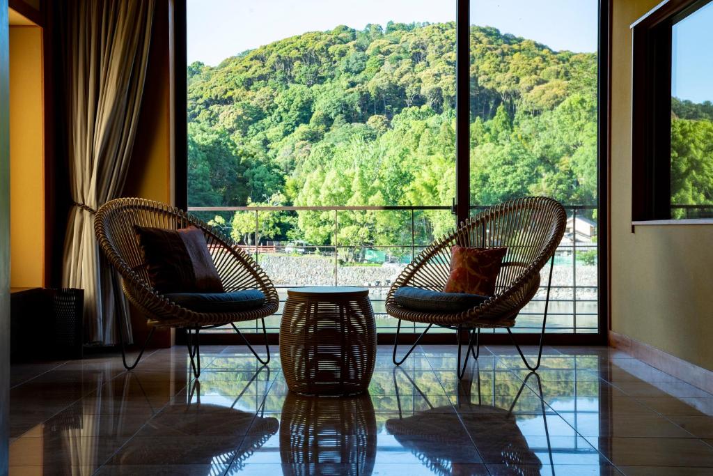 two chairs and a table in front of a large window at Hanayashiki Ukifune-en in Uji