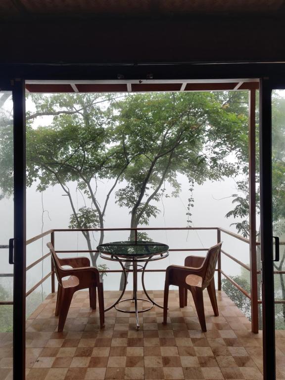 a table and chairs on a balcony with a tree at Sunset Valley Kerala - Where Every Evening Unveils a Perfect Sunset with Private Waterfalls in Pīrmed