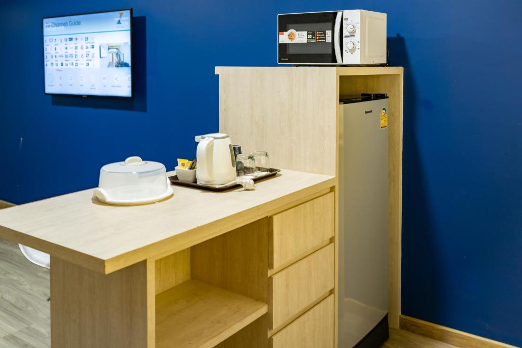 A kitchenette counter with a microwave, mini-fridge, kettle and covered serving dish.