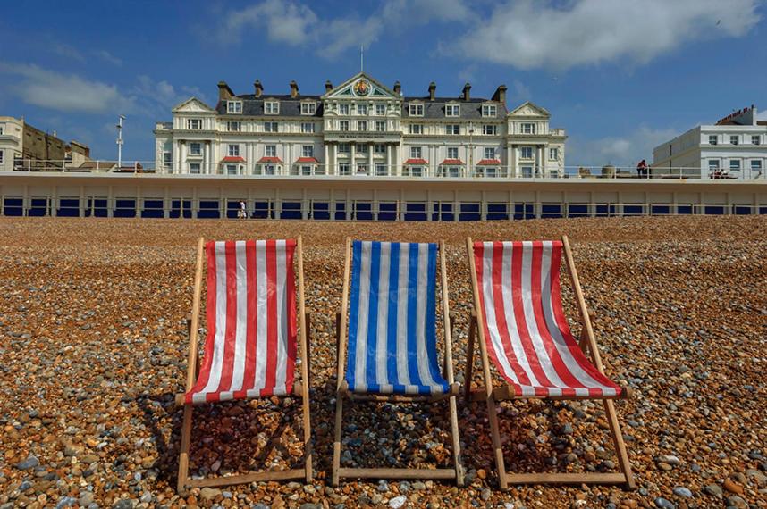 2 chaises assises sur une plage en face d'un bâtiment dans l'établissement Royal Victoria Hotel, à Hastings