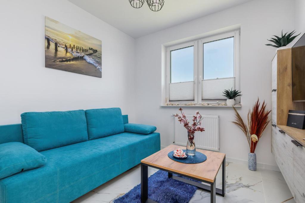 ein Wohnzimmer mit einem blauen Sofa und einem Tisch in der Unterkunft Sea Resort Kropli Bałtyku Apartment with Terrace by Renters in Darłowo