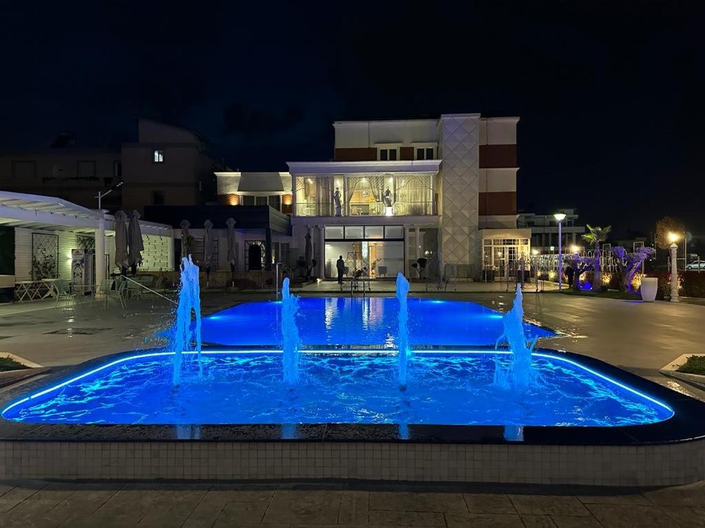 a blue fountain in front of a building at night at Hotel Colis in Tirana
