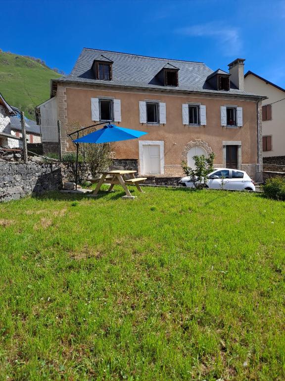 - une table de pique-nique avec un parasol bleu en face d'une maison dans l'établissement Magnifique Cottage à Lescun, à Lescun