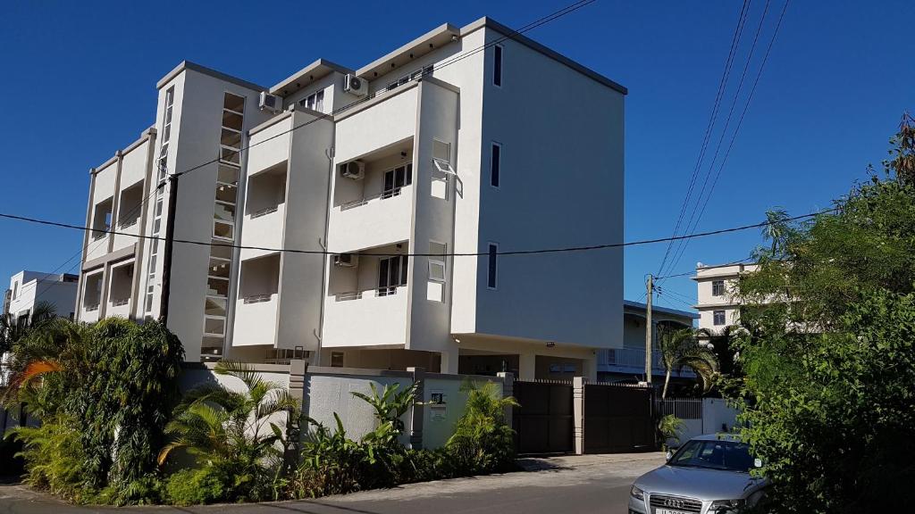 un edificio blanco con un coche aparcado delante de él en Monalysa St Honore Apartment & Studios Grand Bay, en Grand Baie