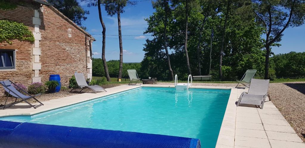 - une piscine avec des chaises et un bâtiment en briques dans l'établissement Gîte Périgourdin la Picherie, à Montpon-Ménestérol