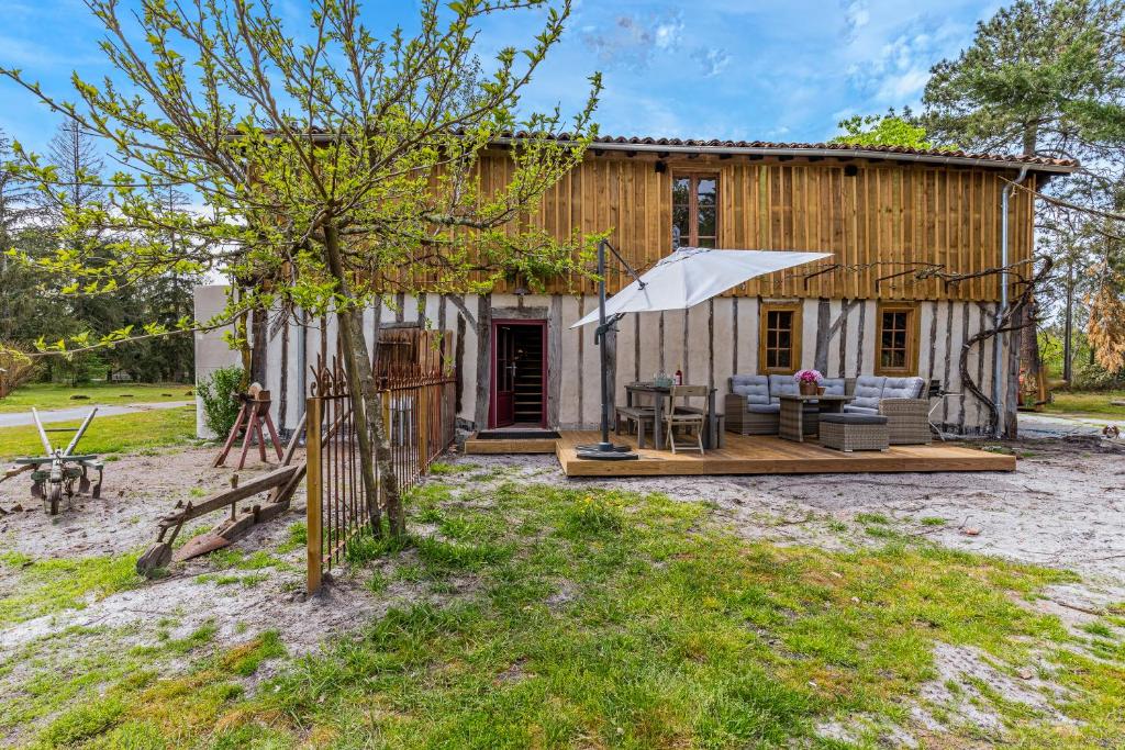 een houten huis met een patio en een parasol bij La grange in Trensacq