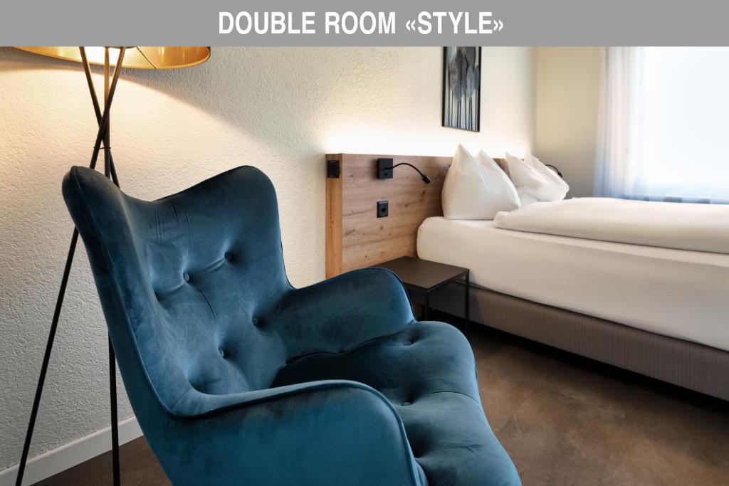 a blue chair in a hotel room with a bed at Hotel Bären Suhr in Aarau