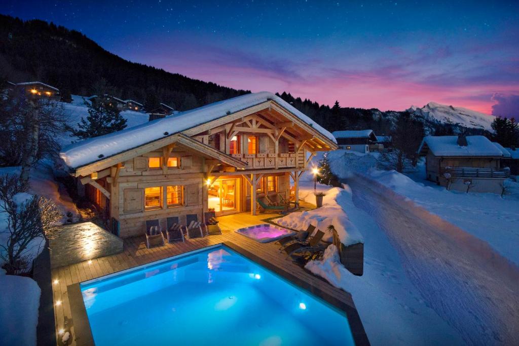 a log cabin with a swimming pool in the snow at Chalet Beauvoir 12 - OVO Network in Saint-Jean-de-Sixt