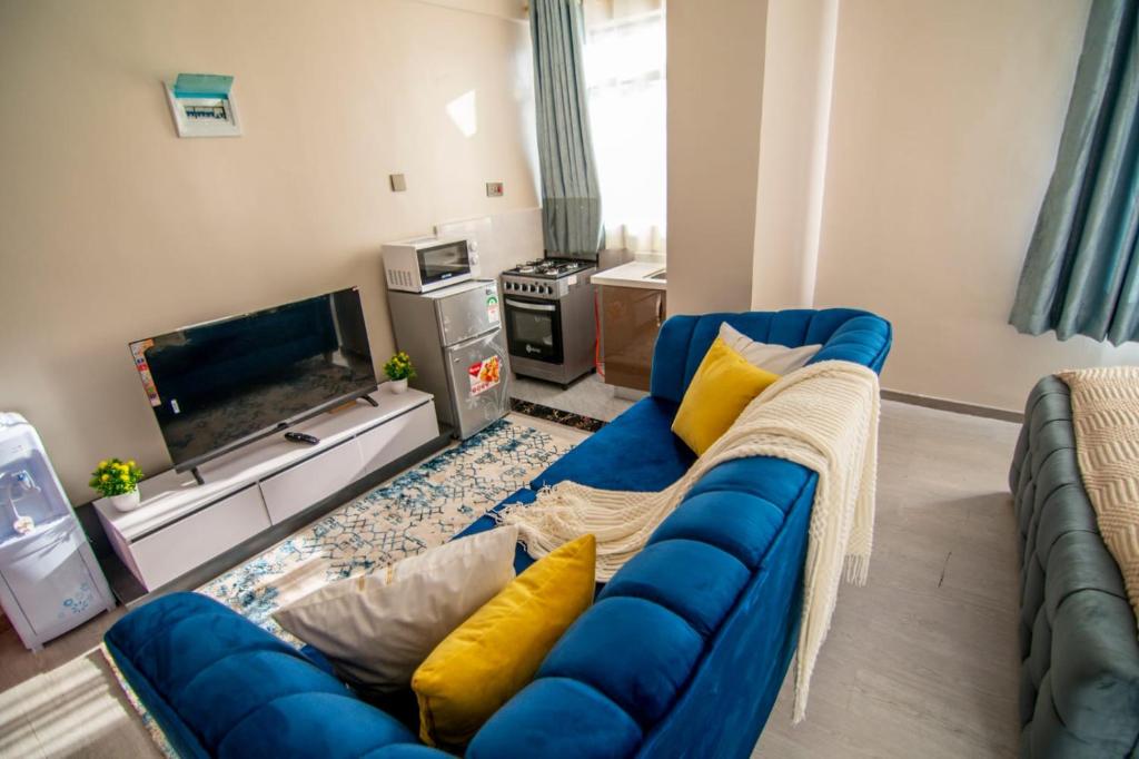 a living room with a blue couch and a tv at Lux Suites Royal Gardens Studio Apartments in Nairobi