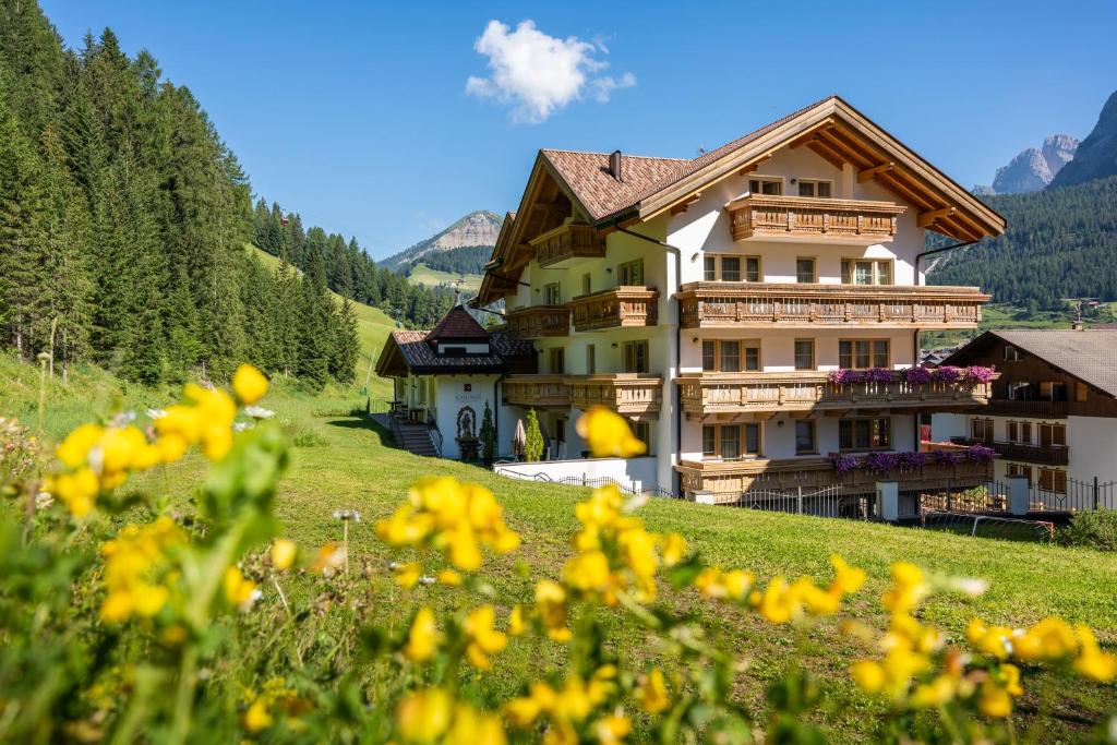 una casa su una collina con fiori gialli in primo piano di Hotel Somont a Selva di Val Gardena