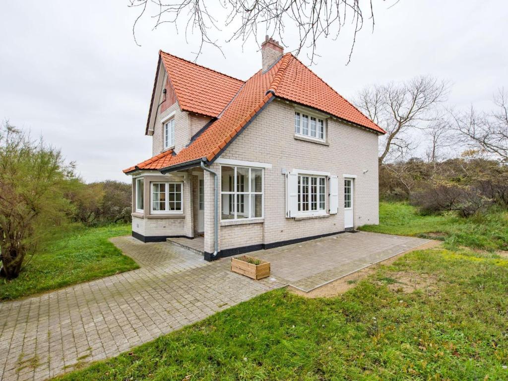 ein kleines weißes Haus mit orangefarbenem Dach in der Unterkunft Renovated Hortensia Villa with a unique location next to the dunes in Koksijde