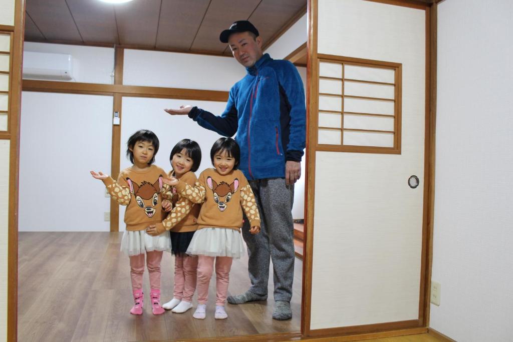 un hombre y dos niños parados en una habitación en JR福井駅東口から徒歩7分(550m)。一棟貸切民泊トリプレッツ en Fukui
