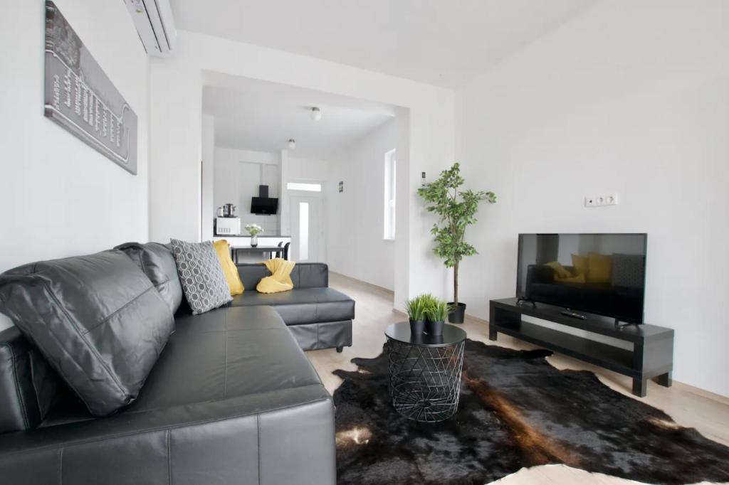 sala de estar con sofá de cuero negro y TV de pantalla plana en Family Apartments by Hi5 - Zamardi, en Zamárdi