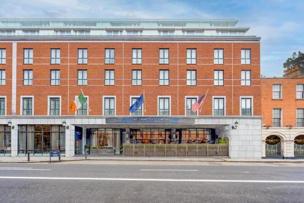 een groot gebouw van rode baksteen met vlaggen voor het gebouw bij The Trinity City Hotel in Dublin