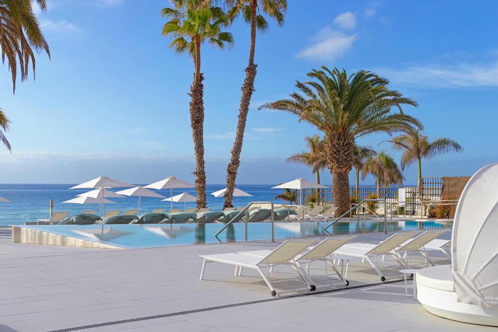 a pool with chairs and palm trees and the ocean at Paradisus by Meliá Gran Canaria - All Inclusive in San Agustin