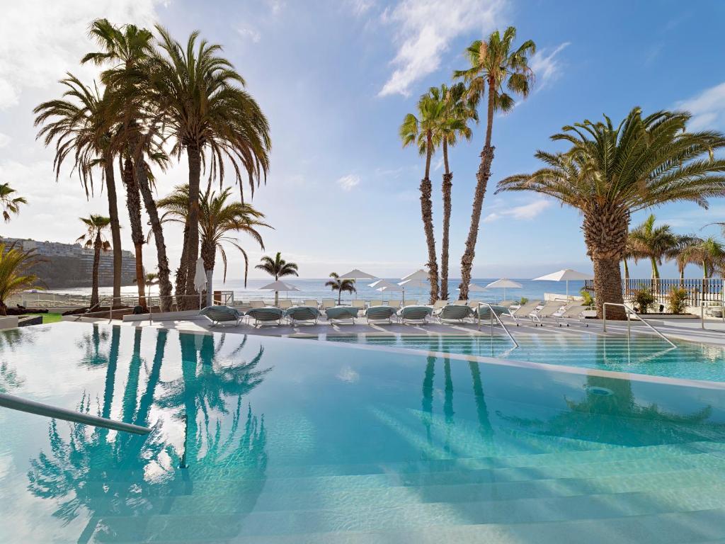 a large swimming pool with palm trees and the ocean at Paradisus Gran Canaria in San Agustin