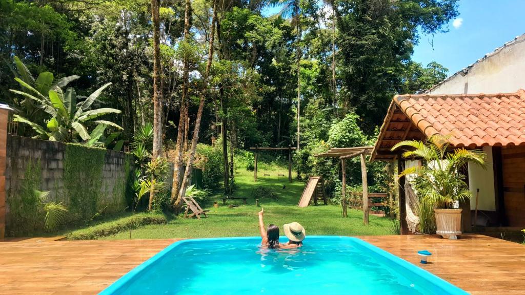 two people in a swimming pool in a backyard at Chalé Aconchegante com Piscina in Penedo