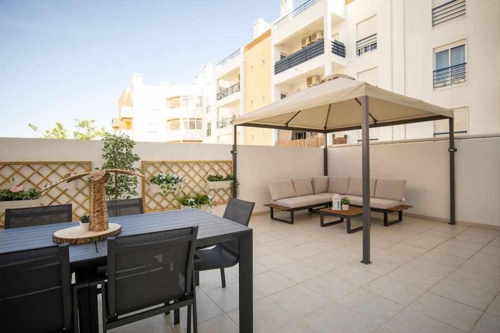 um pátio com um guarda-sol, uma mesa e cadeiras em Modern 3br Apt w/ Lg Terrace, Bbq, Ac & Parking em Tavira