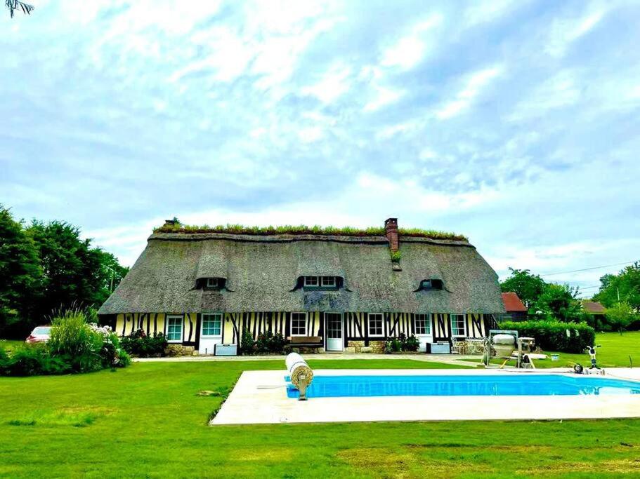 una casa grande con techo de paja y piscina frente a ella en Chaumière de charme cosy, en Saint-Éloi-de-Fourques