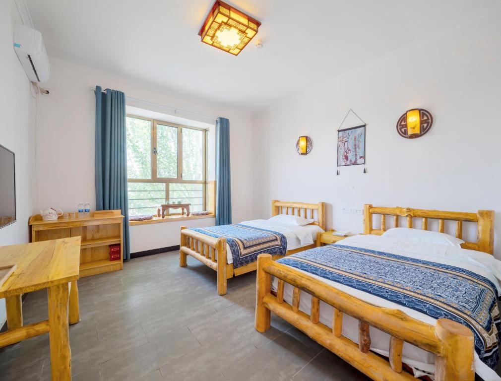 a bedroom with two beds and a table and a window at Dunhuang Hu Yang Inn in Dunhuang