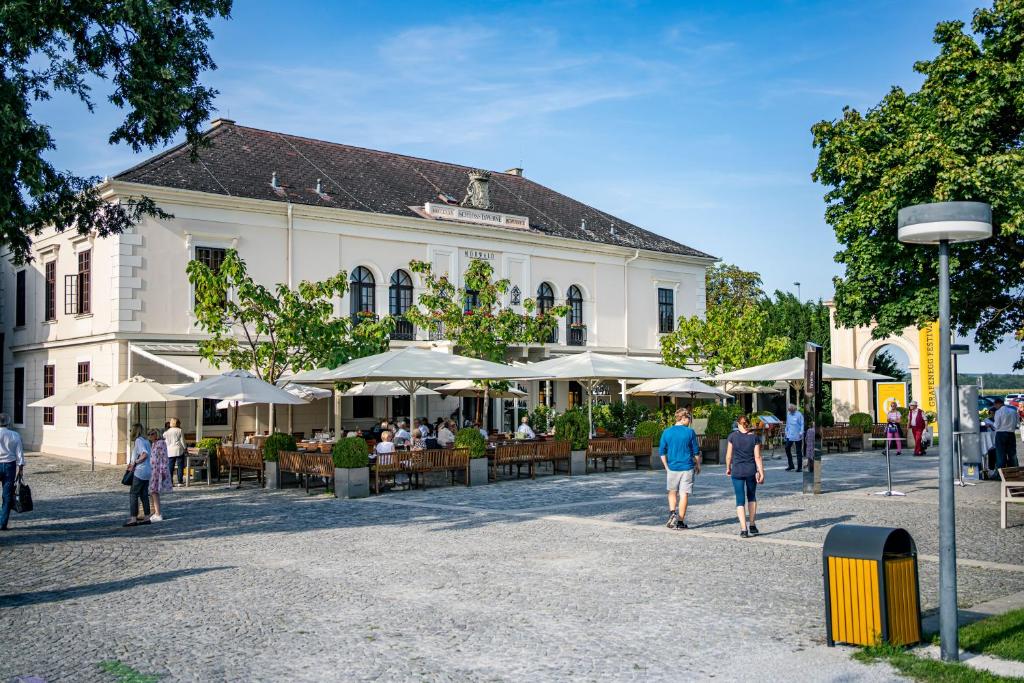 Menschen, die vor einem Gebäude mit Tischen und Sonnenschirmen spazieren in der Unterkunft MÖRWALD Grafenegg Hotel in Grafenegg