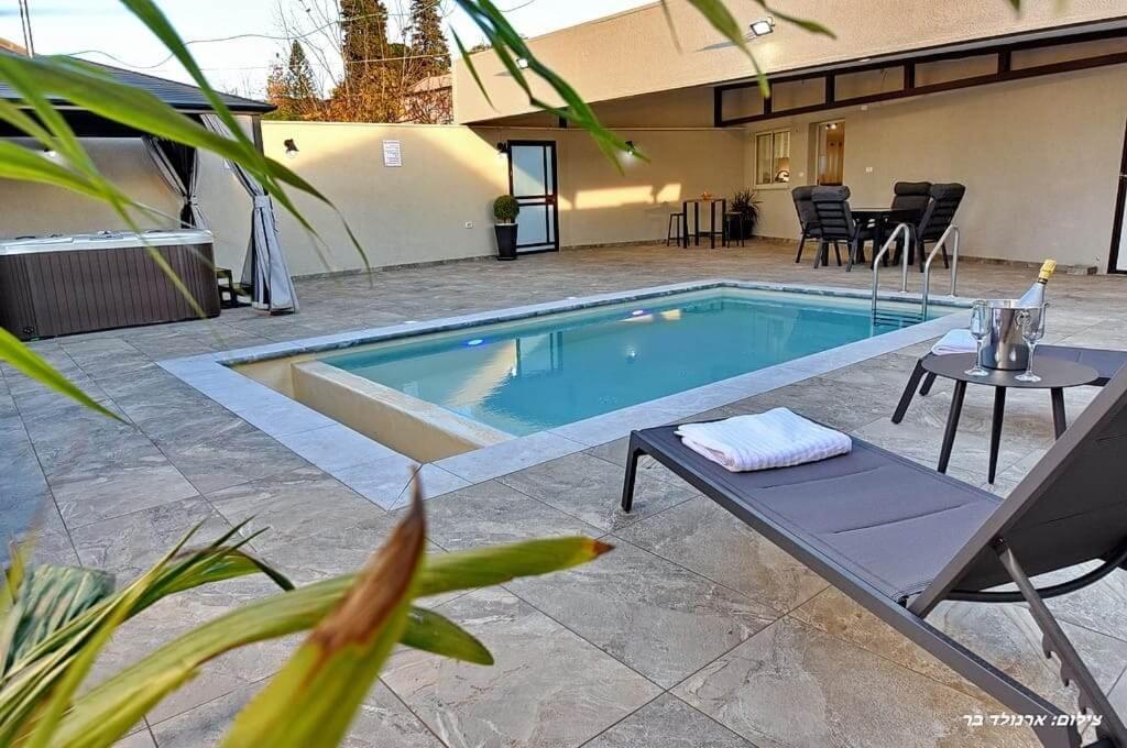 una piscina en un patio con mesa y patio en שרדונה - סוויטה מהממת עם ג'קוזי ובריכה פרטית מחוממת ומקורה, en ‘Ein Ya‘aqov