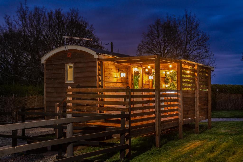 a wooden tiny house with lights in the yard at Hillside View Shepherds Hut - Ockeridge Rural Retreats in Little Witley