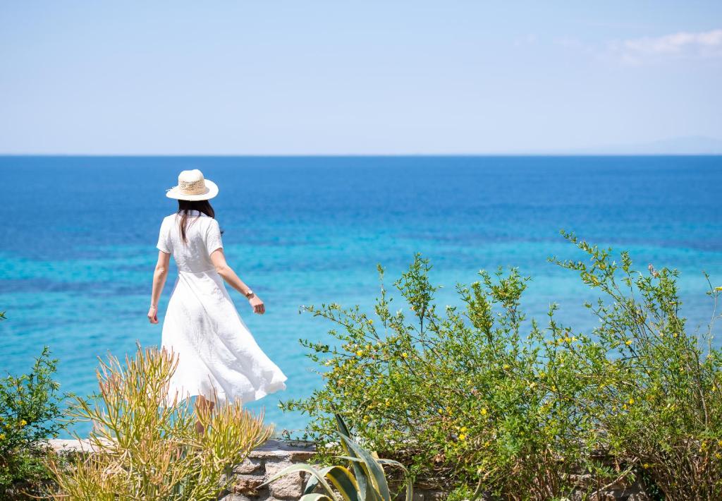 a woman in a white dress walking along the ocean at Stone-Home Living in Neos Marmaras