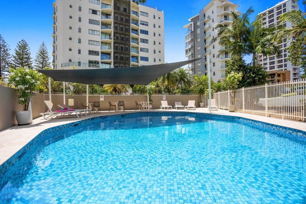 uma grande piscina com mesas, cadeiras e edifícios em Two Bedroom Ocean View Penthouse at Pelican Sands em Gold Coast