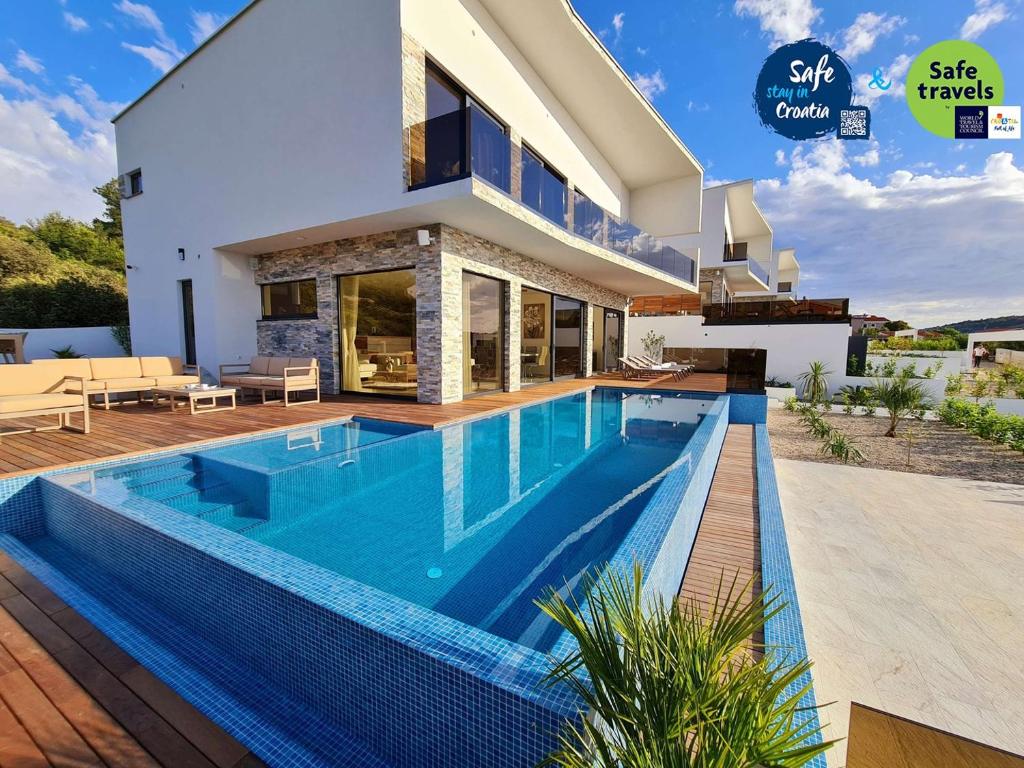 une villa avec une piscine en face d'une maison dans l'établissement Villa Ramarin III with infinity heated pool, jacuzzi and sauna by the sea in Rogoznica, à Rogoznica