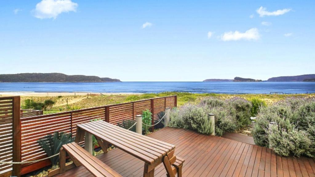 a wooden deck with a bench and a view of the ocean at Beachcomber - Waterfront Umina Beach Wifi in Umina