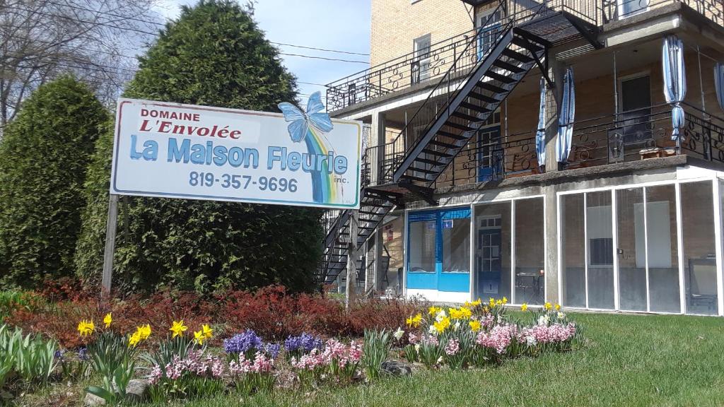 un cartel delante de una casa con flores en MHotel Domaine l'Envolée- Maison Fleurie, en Victoriaville